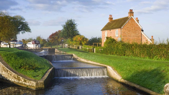Two small weirs with a red brick house on the right bank and blue skies above
